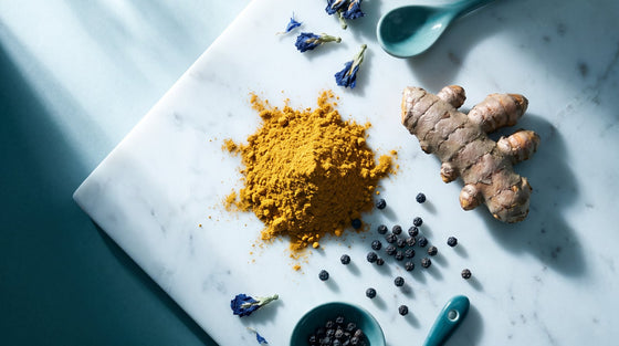 Golden turmeric powder and root with scattered black peppercorns, a macro flat lay highlighting turmeric and black pepper absorption.