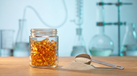 Amber supplement capsules and collagen powder in warm light with blurred laboratory glassware behind, evoking supplement quality and regulation.