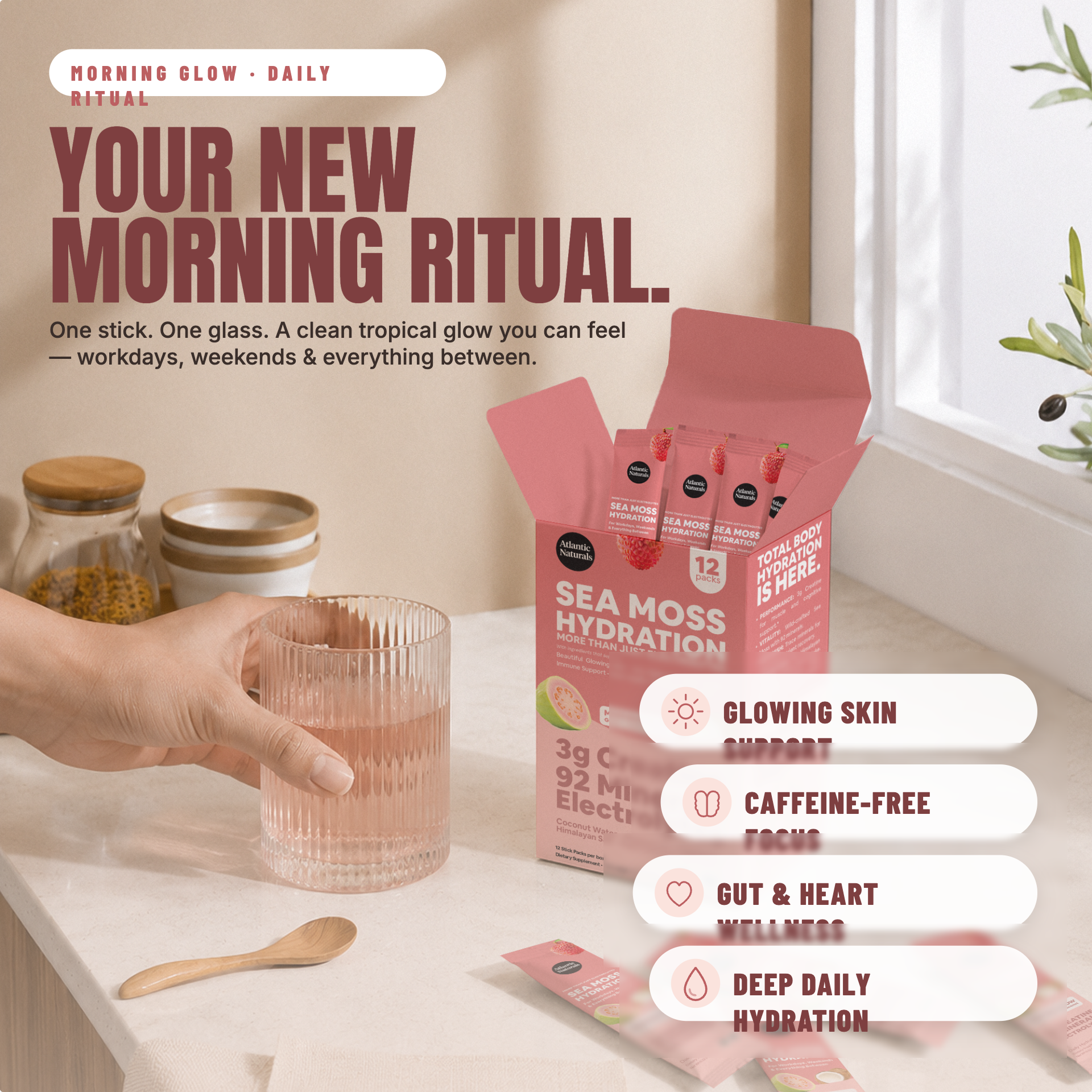 A hand holds a glass over a pink sea moss hydration powder box on a light countertop. The box is pink with black text and shows 12 individual stick packs inside. morning glow